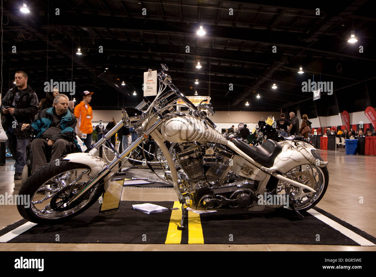 A customized motorcycle or chopper with custom paint job on display and for sale in a show room with customers looking over it Stock Photo