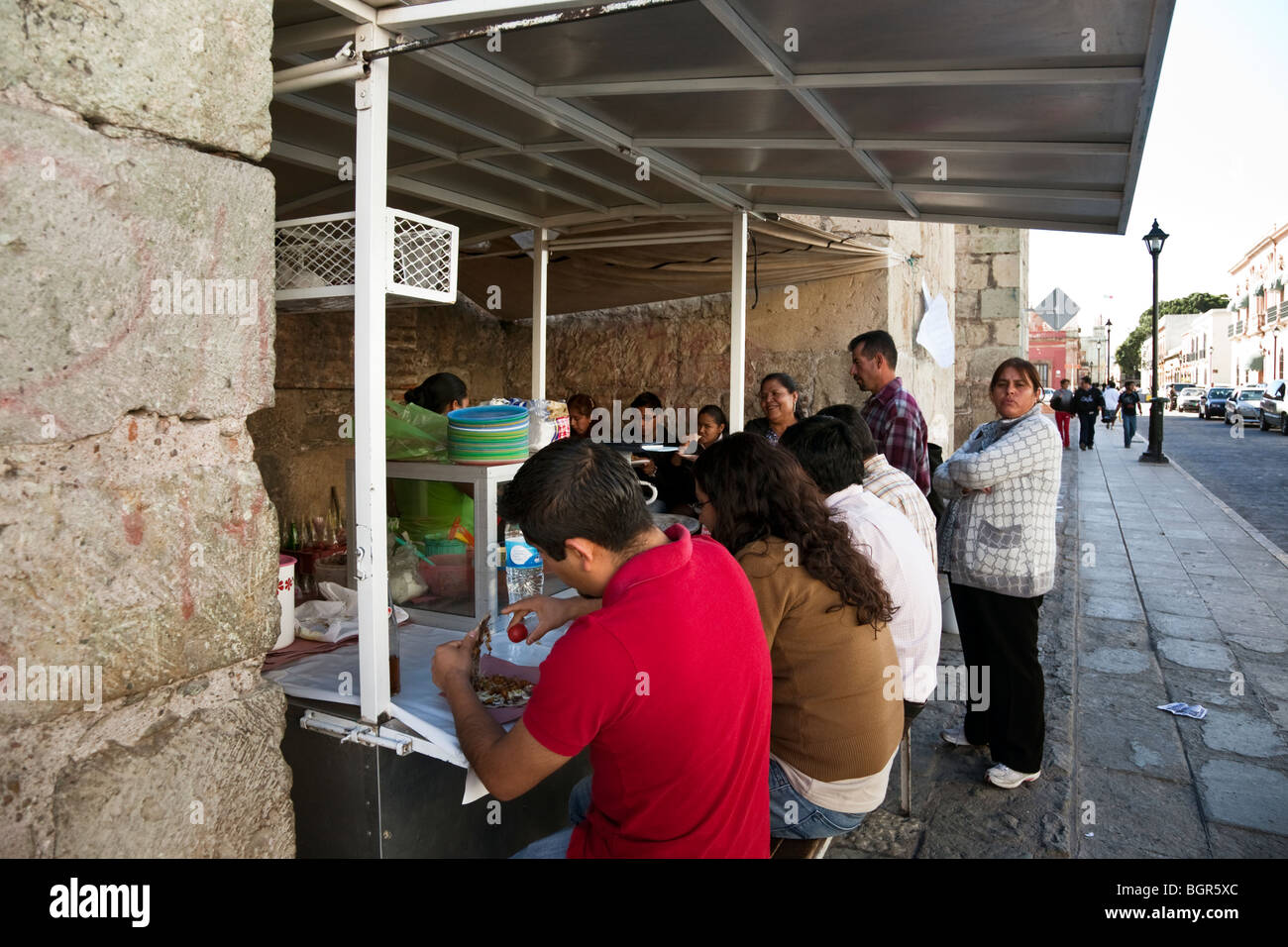 seated customers enjoy their food while those in line wait for their cooking tacos at a street stall booth Oaxaca City Mexico Stock Photo