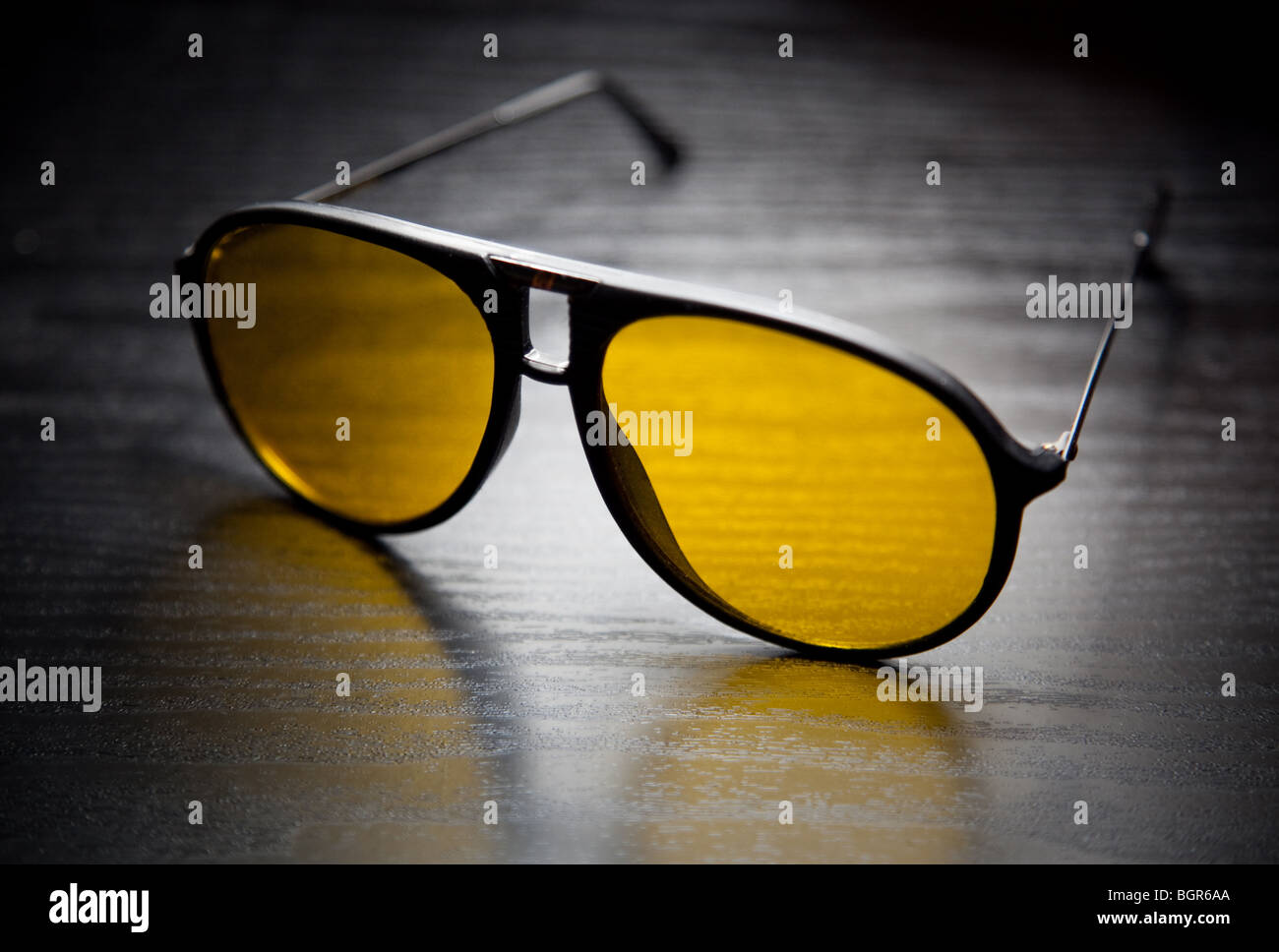 A pair of cool yellow lens sunglasses on a shiny black table Stock Photo