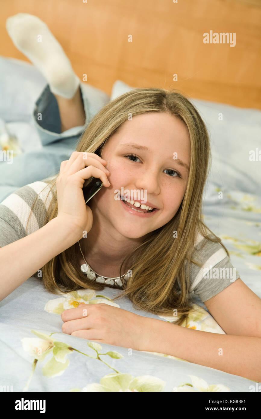 Caucasian preteen girl laying in bed talking on a cell phone Stock Photo