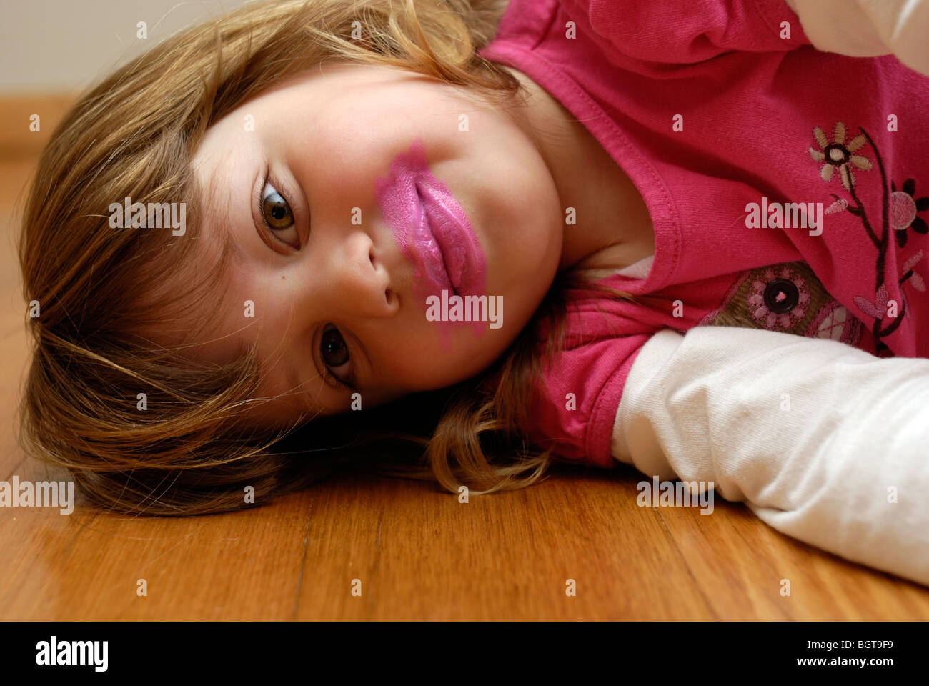 Three year old girl playing with pink lipstick makeup Stock Photo