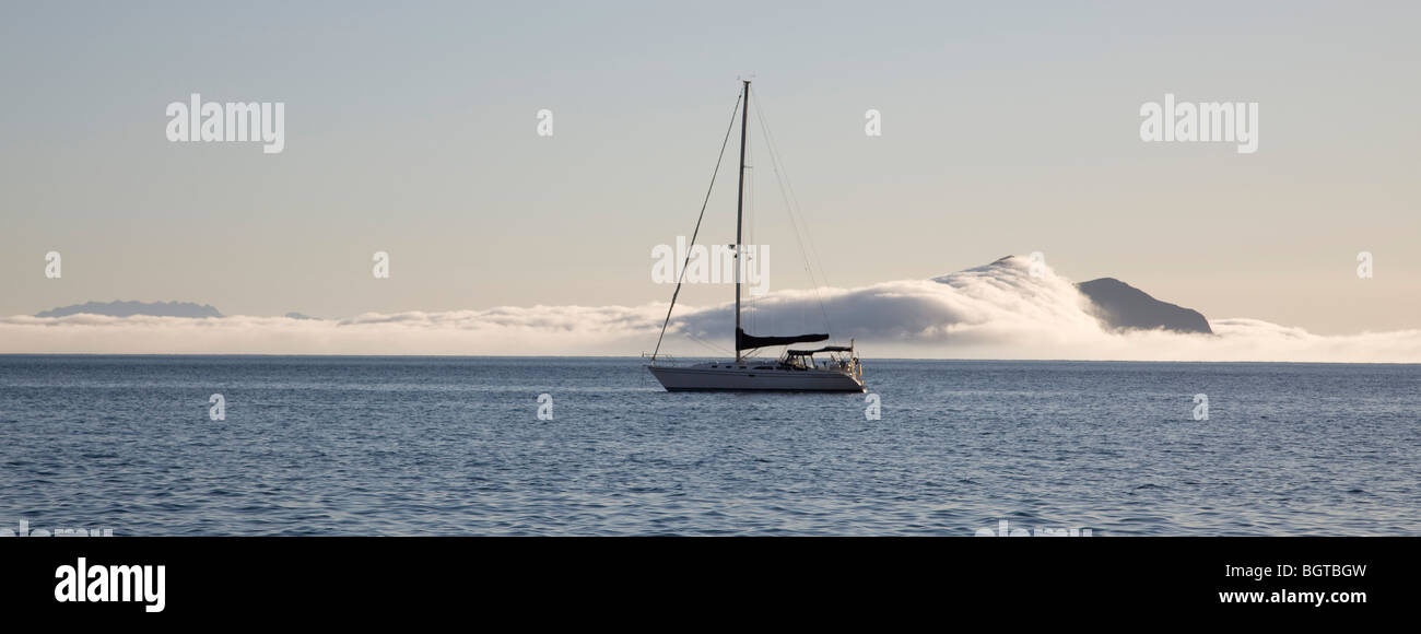 Sailboat anchored by fog covered island in pacific ocean Stock Photo