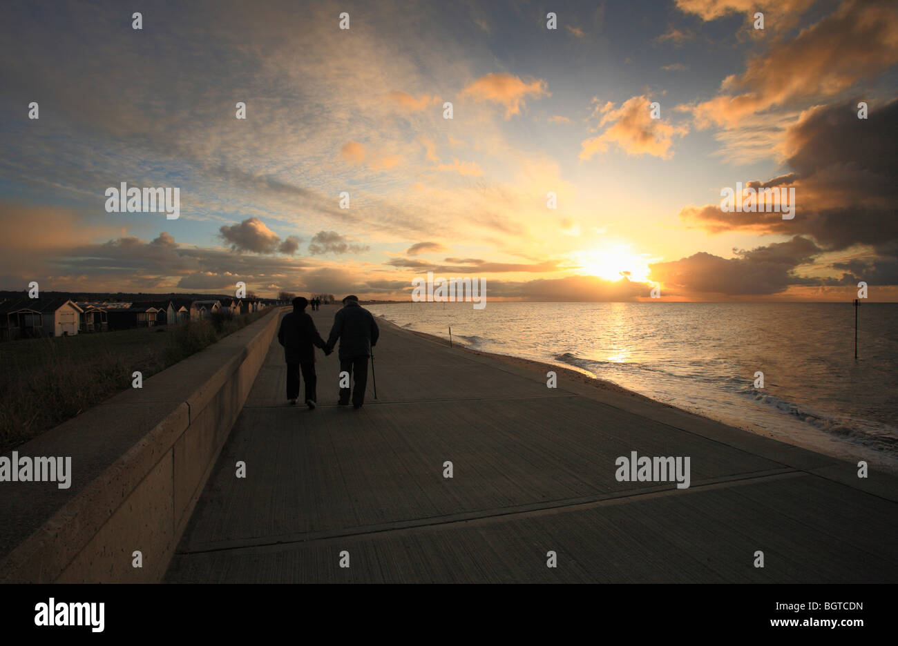 An elderly couple walk hand in hand along the seafront at Heacham, Norfolk at sunset. Stock Photo