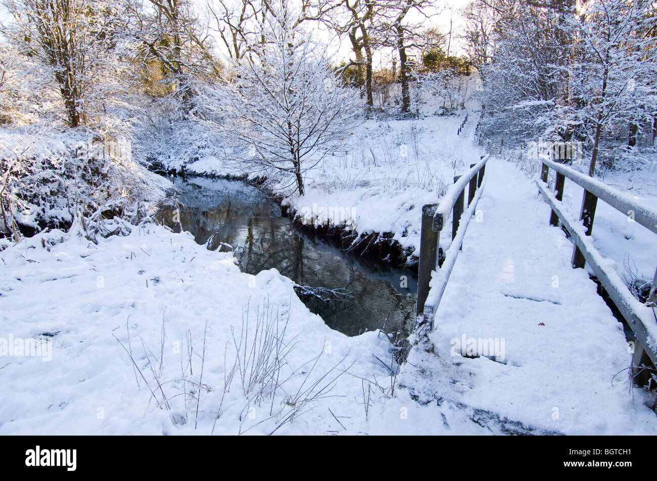 A makeshift wooden bridge taking a footpath over a small river during the winter with fresh snow on the ground. Stock Photo