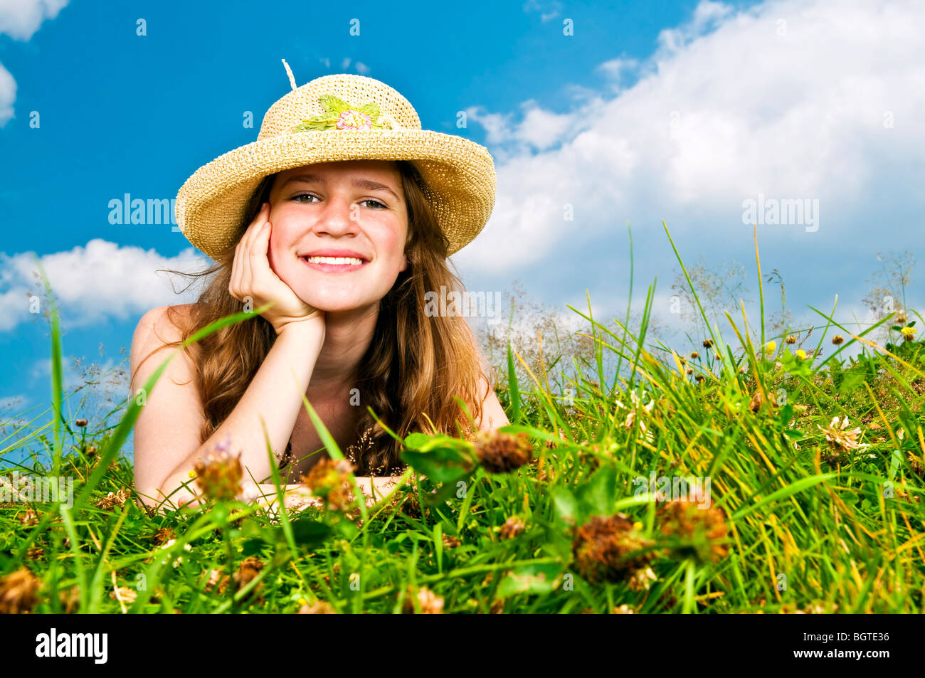 Young teenage girl laying in summer meadow resting chin on hand in straw hat Stock Photo