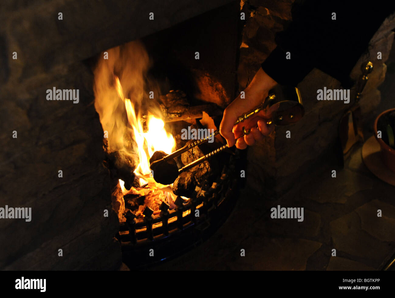 A piece of coal is put on to an open fire using tongs UK Stock Photo