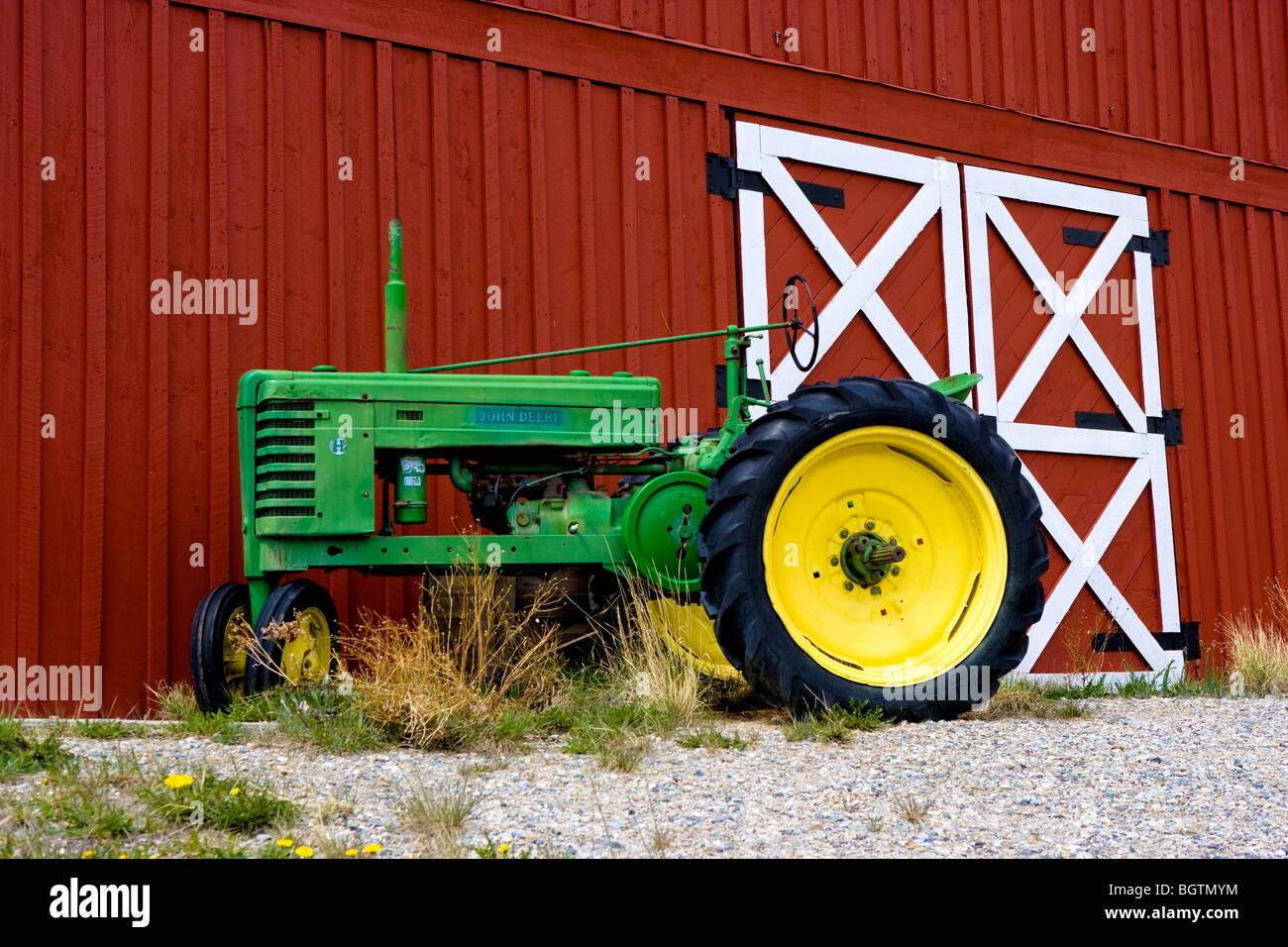 Green vintage John Deere tractor with yellow wheels parked against red barn Stock Photo