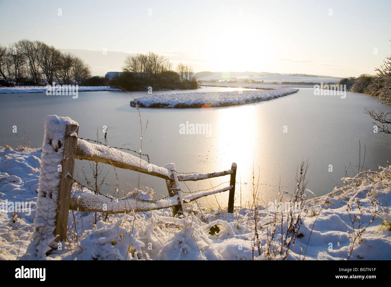 A winter scene at Cuckmere Valley of snow covered fence, frozen river and sunshine. Stock Photo