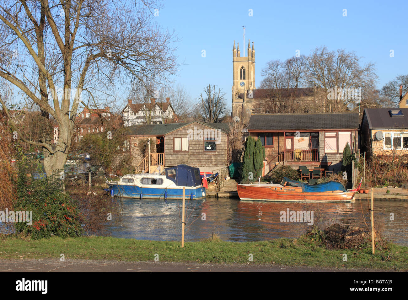 Boats and holiday homes on Garrick's Ait island, River Thames, East Molesey, England, UK, Europe. Hampton church on other side of river in background. Stock Photo