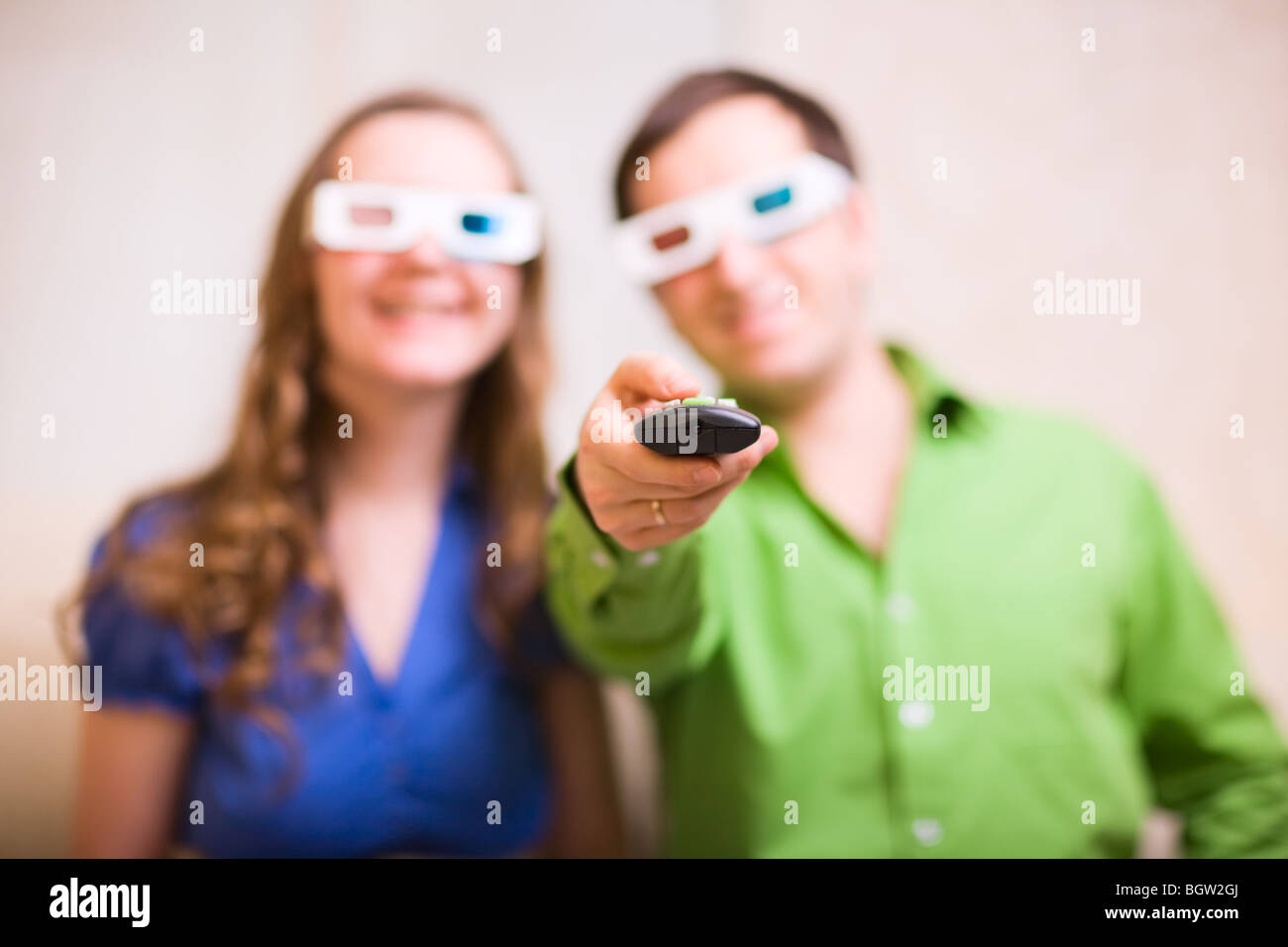Young couple at home watching movie in 3D glasses. Focus on remote control.  Stock Photo