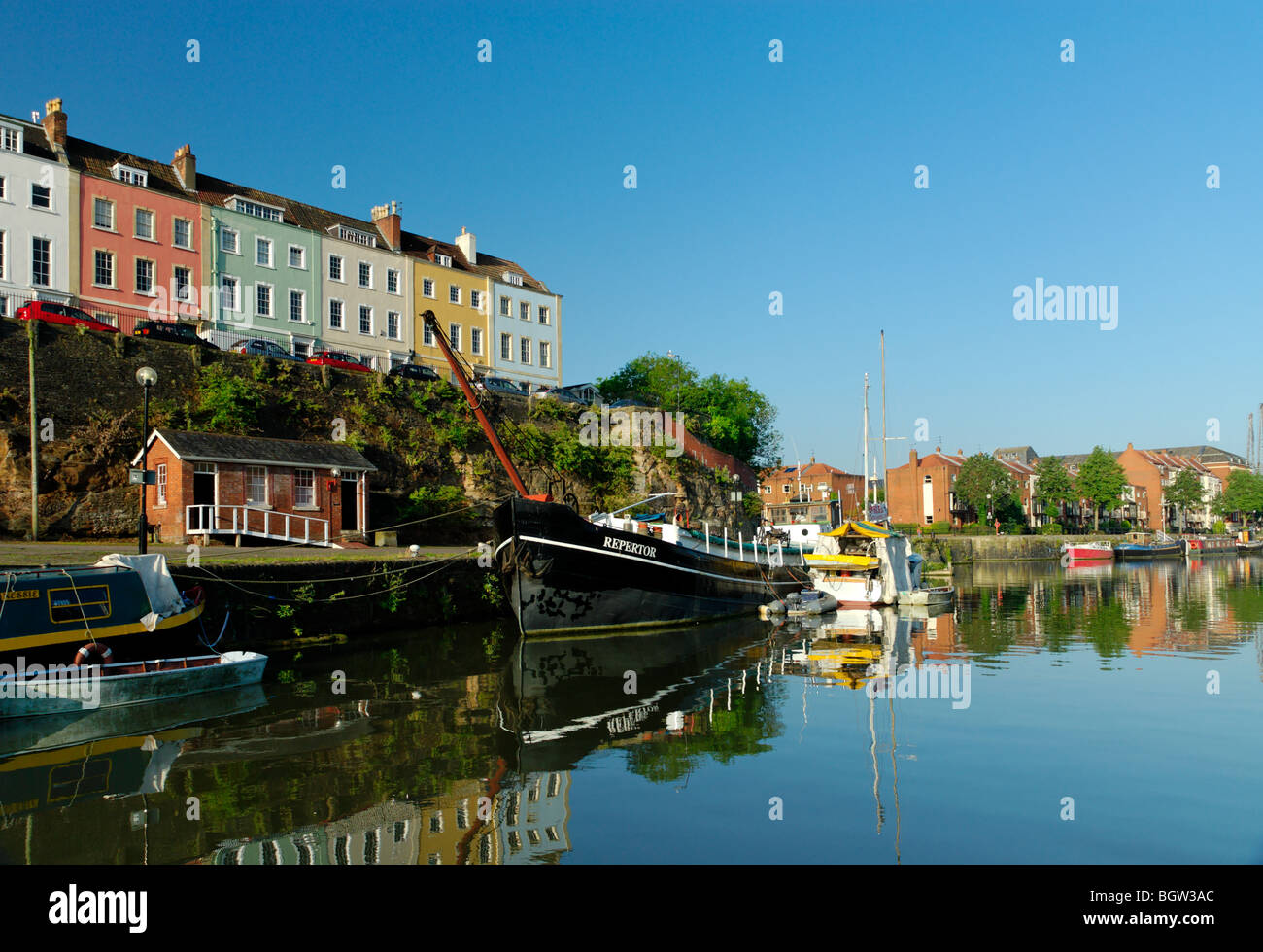 Painted multicoloured Georgian houses atop a steep cutting above Bristol city historic docks with deep blue clear sky. Stock Photo