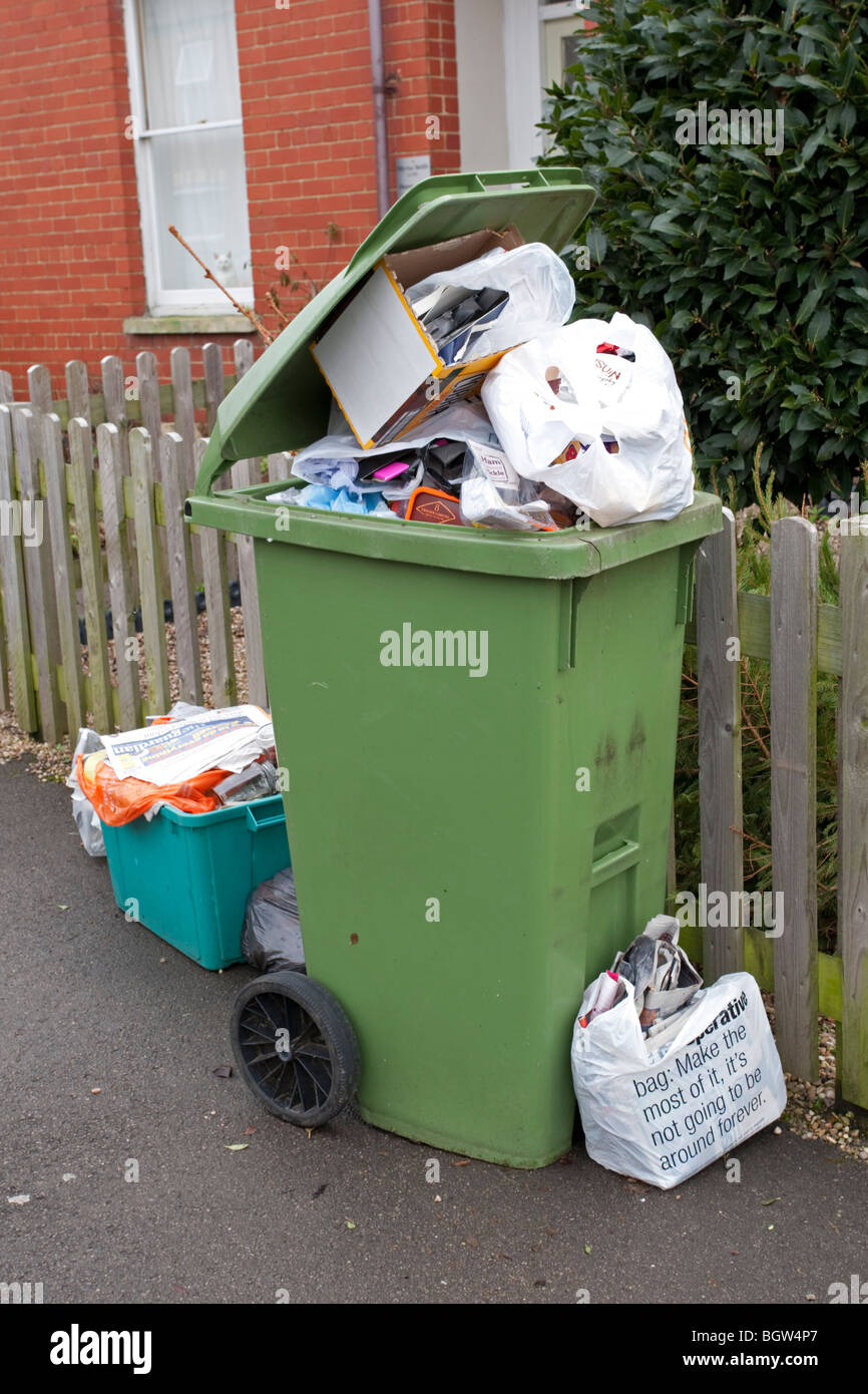 Green wheelie bin overflowing with domestic rubbish awaiting collection Cheltenham UK Stock Photo