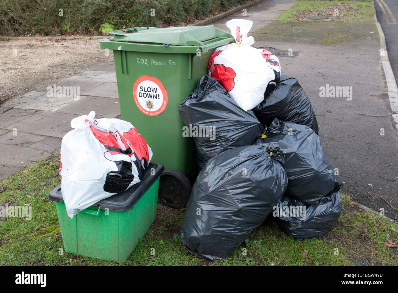 Green wheelie bin overflowing with domestic rubbish awaiting collection
