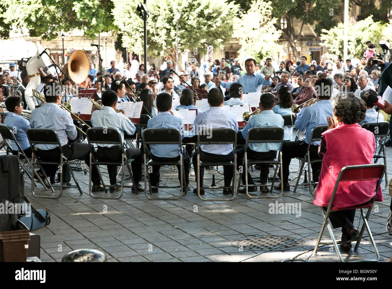 seated orchestra members & conductor during well attended concert in the Zocalo on a sparkling Sunday in Oaxaca City Mexico Stock Photo