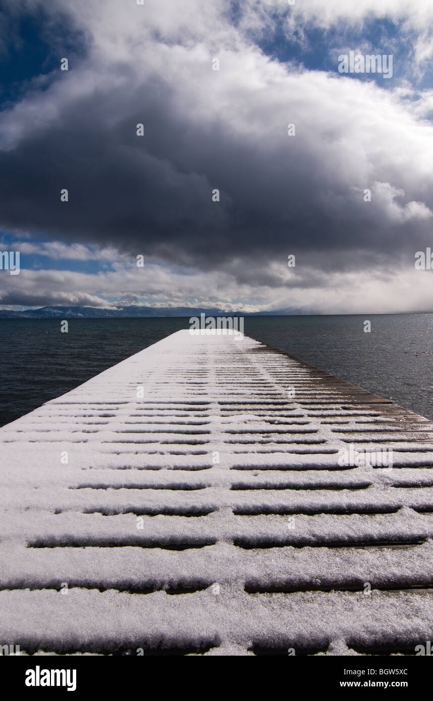 A snow covered pier in winter with clouds in the sky on Lake Tahoe in California Stock Photo