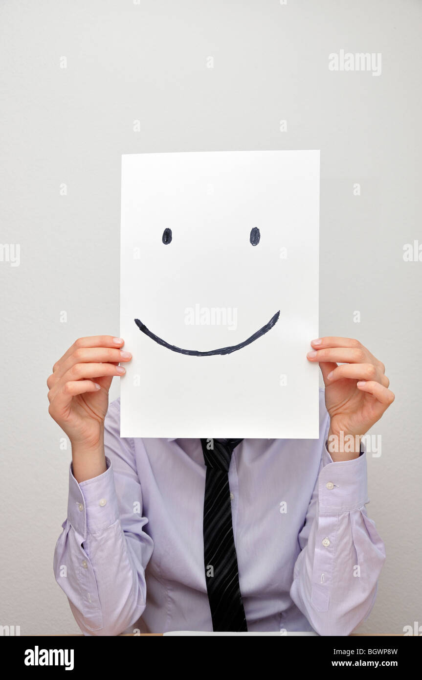 Businesswoman holding card with smiley face in front of face Stock Photo