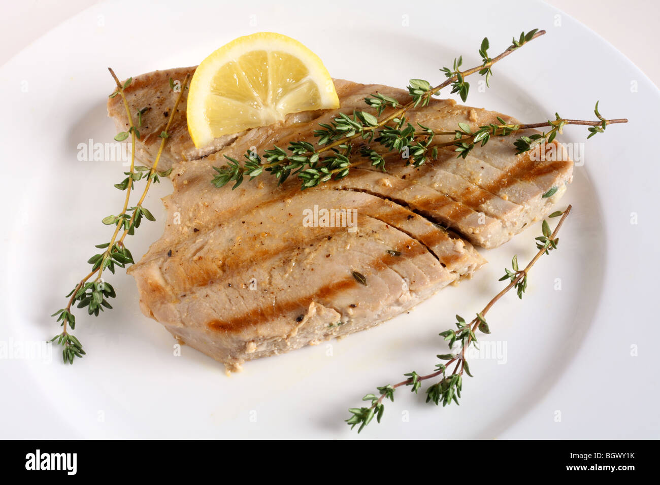 A grilled tuna steak, garnished with sprigs of thyme, on a plate with a