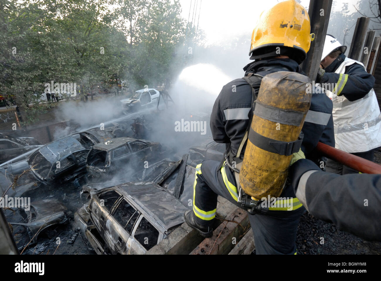 Firemen uses hose at scrapyard car fire Stock Photo