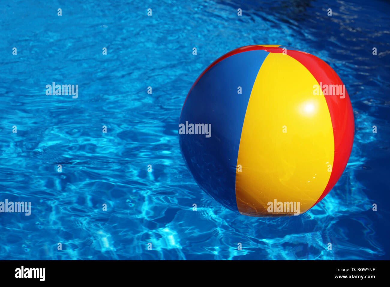 An inflatable colored plastic ball swimming in a shiny blue swimming pool. Stock Photo