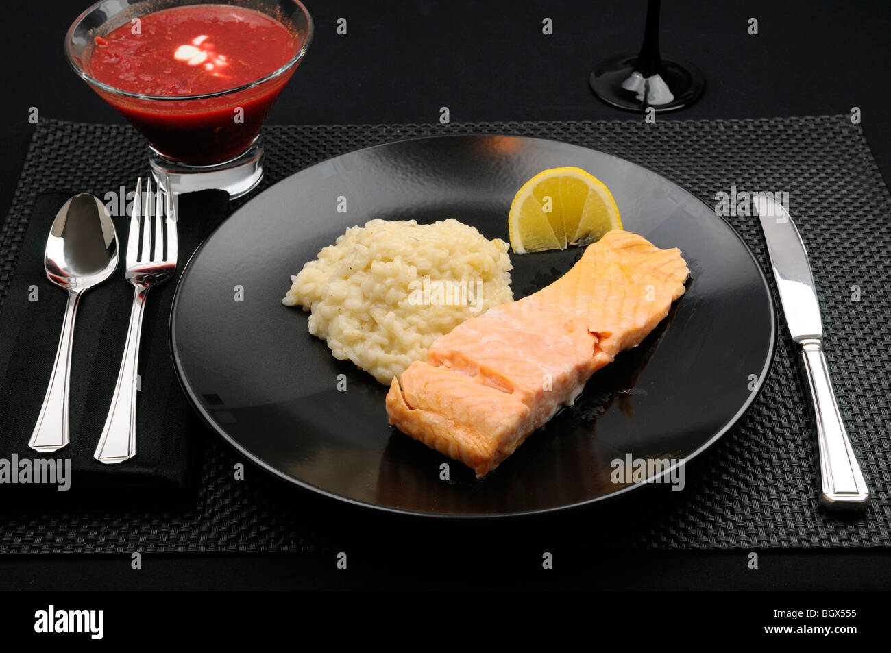 Black table setting with plate of salmon lemon and risotto with borscht soup Stock Photo