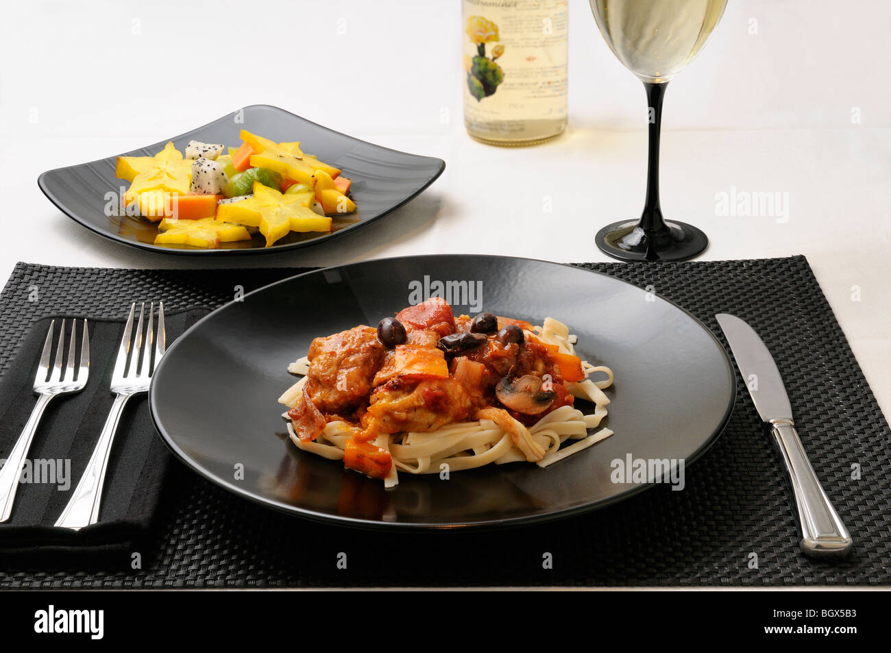 Table setting with plate of Chicken Marengo with fruit salad and white wine Stock Photo