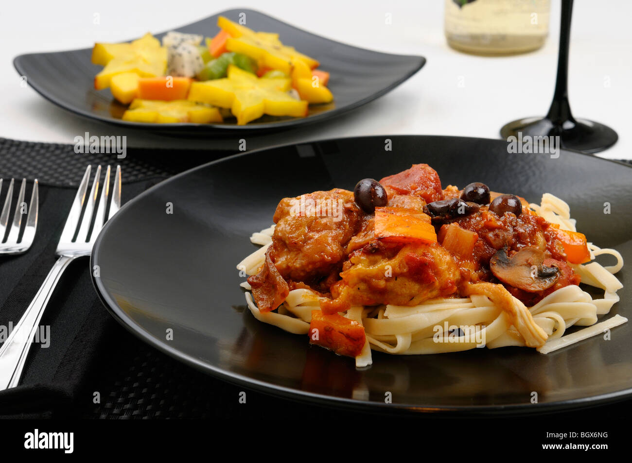 Close up of table setting with plate of Chicken Marengo with fruit salad and white wine Stock Photo