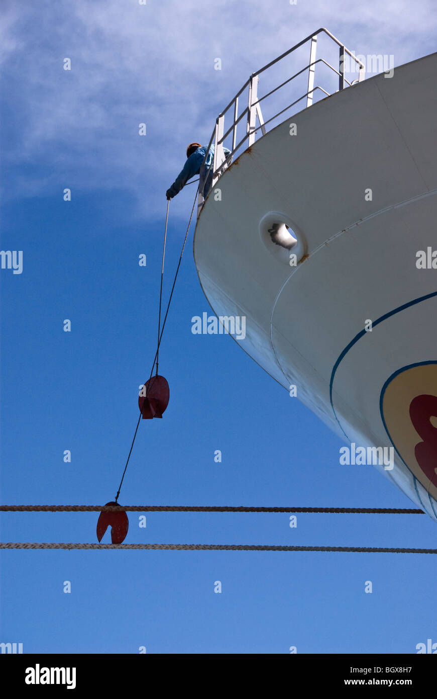 A crewman at the bow of a ship places rat guards on mooring ropes just