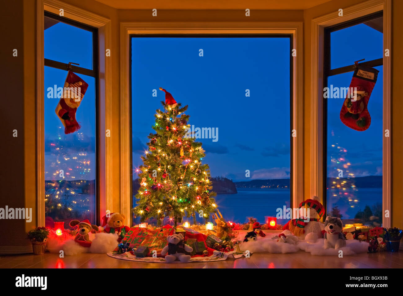 Christmas Tree with lights, decorations, and gifts in a window at dusk, The Artists Point, Hyde Creek, Port McNeill, Northern Va Stock Photo