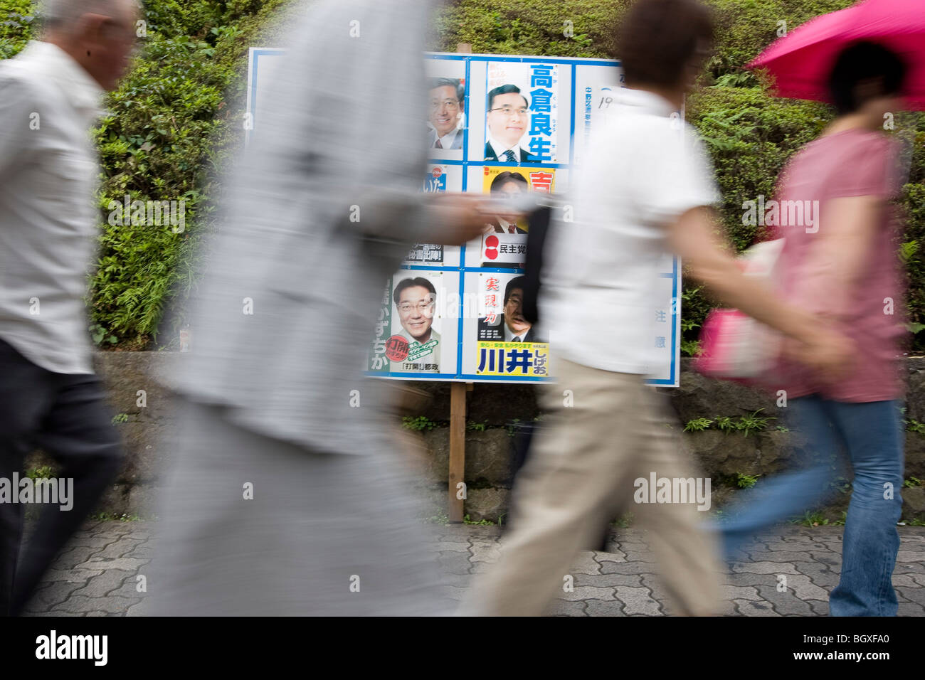 Pedestrians walk past posters for political party candidates, advertising their candidacy for Tokyo Metropolitan elections. Stock Photo