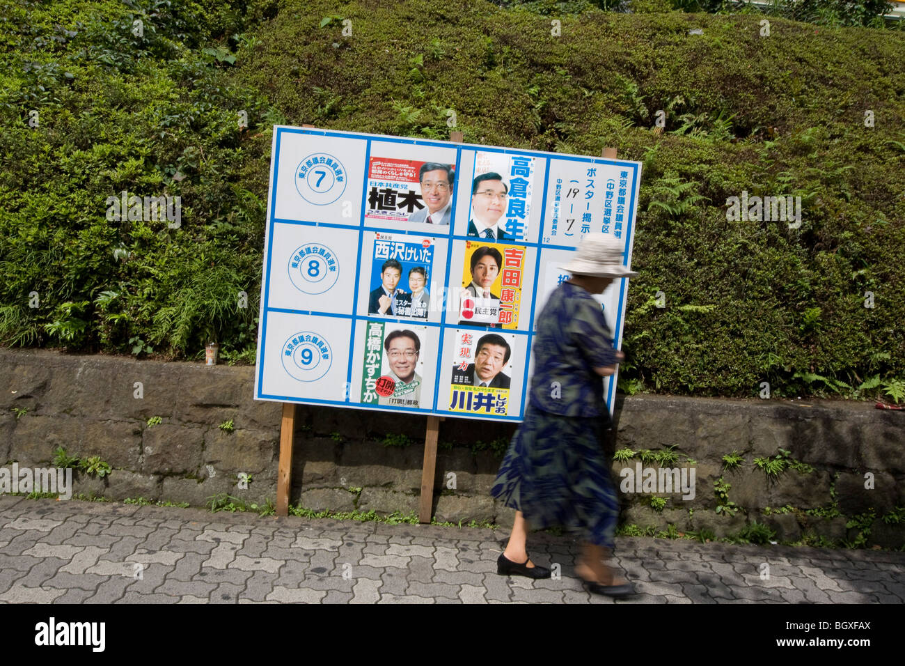 Pedestrians walk past posters for political party candidates, advertising their candidacy for Tokyo Metropolitan elections. Stock Photo