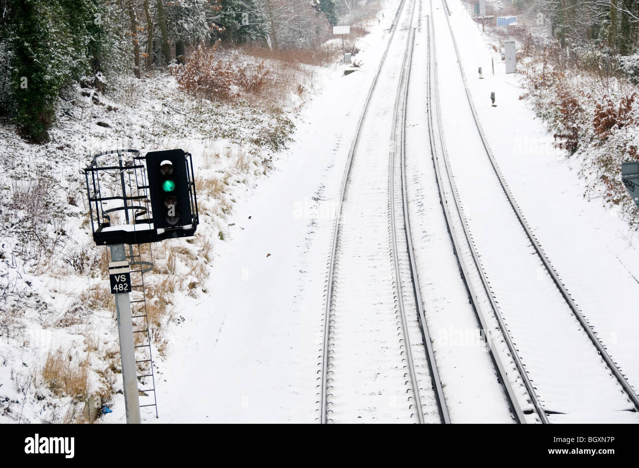 Green light for snow-bound trains?  A green signal with snow-covered railway lines in the background. Stock Photo