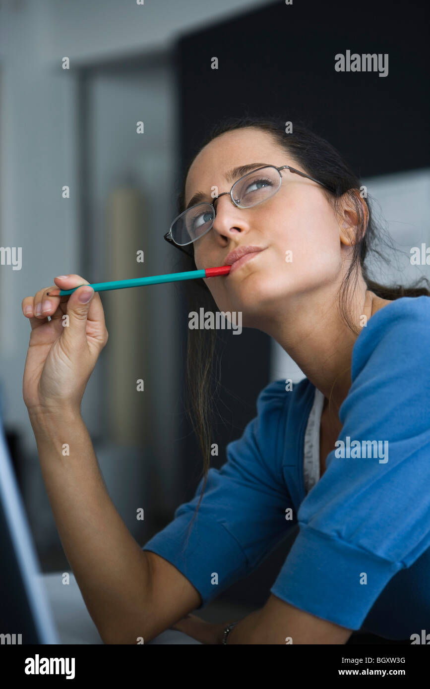 Woman contemplatively looking away with pen in mouth Stock Photo - Alamy