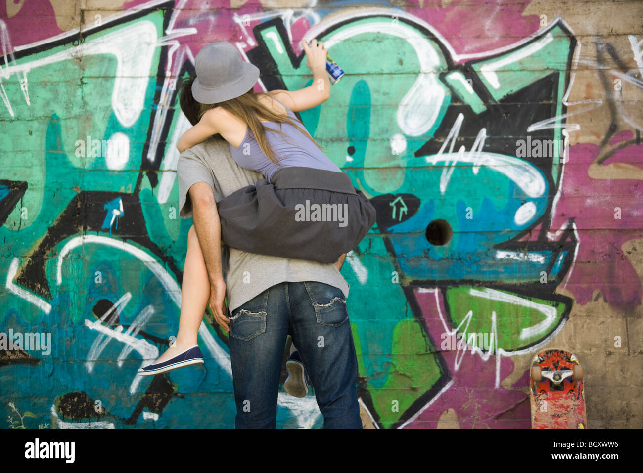 Young woman straddling companions back, spray painting graffiti mural Stock Photo