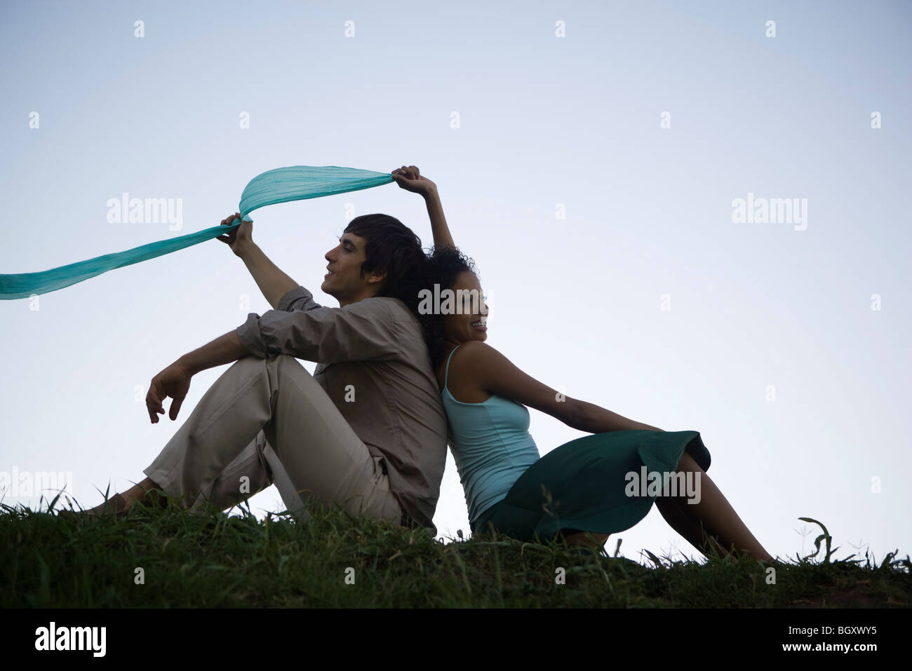 Young couple sitting in grass back to back Stock Photo
