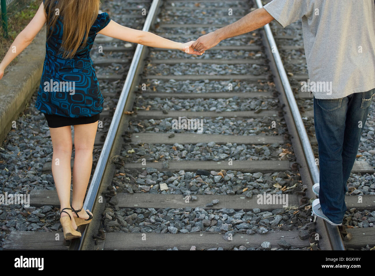 Young couple holding hands walking on rail track, rear view Stock Photo