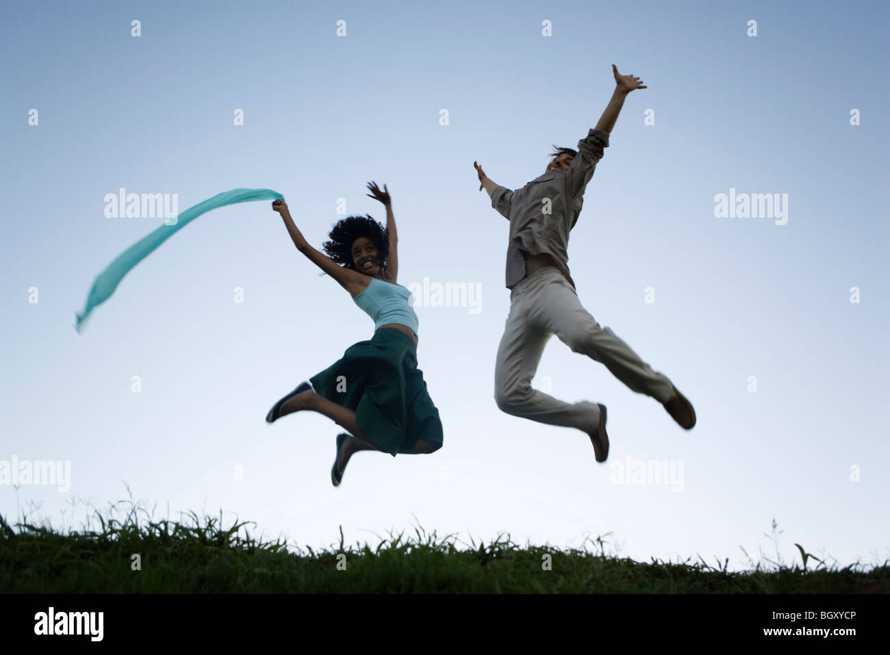 Young couple exuberantly jumping with arms raised wearing expressions of joy Stock Photo