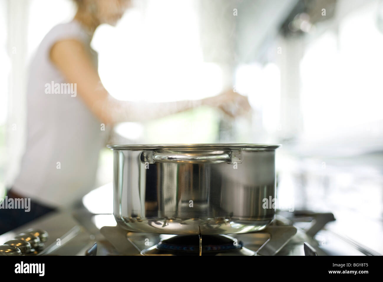 Pot cooking on stove, woman in background Stock Photo