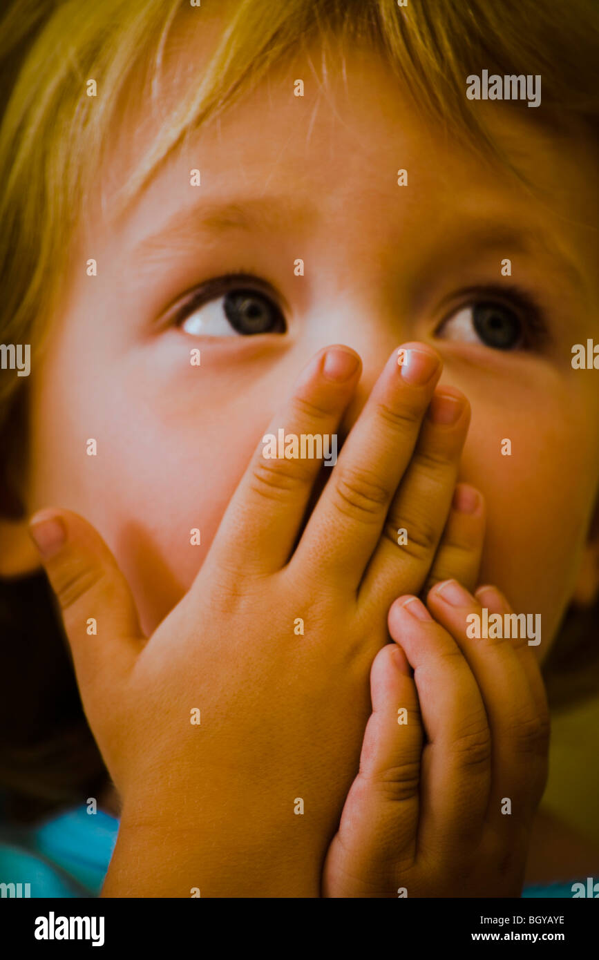 Child covering mouth with hands looking up expectantly Stock Photo