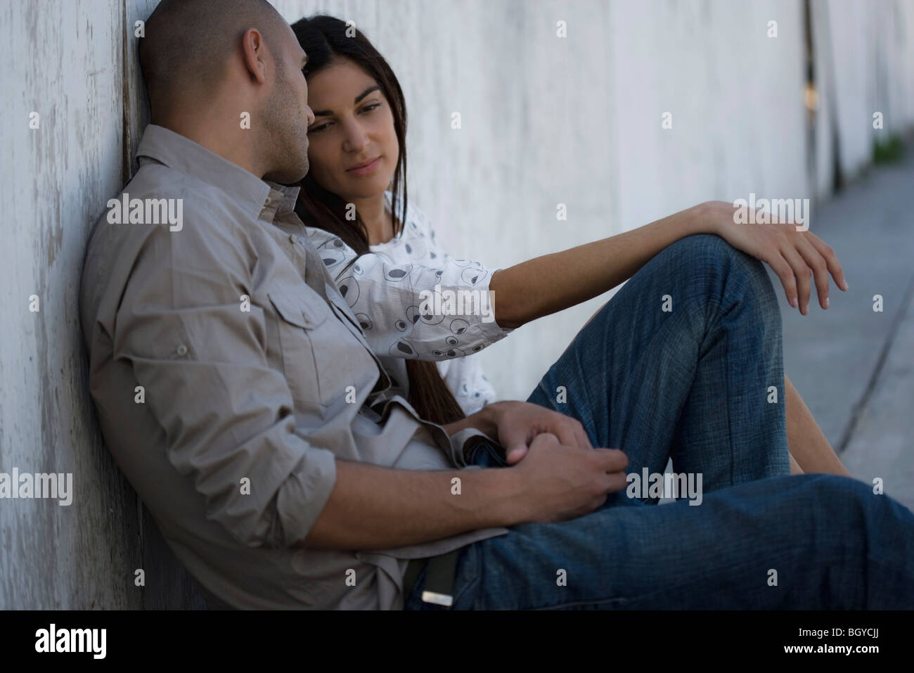 Young Couple Sitting Side By Side On Ground Leaning Against Wall Having Conversation Stock 8602