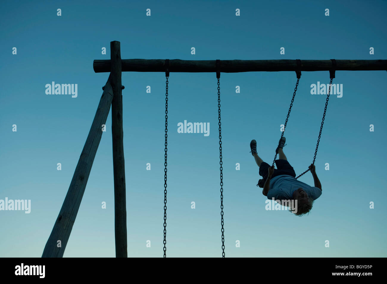 Young man swinging on swing set, backlit Stock Photo Alamy