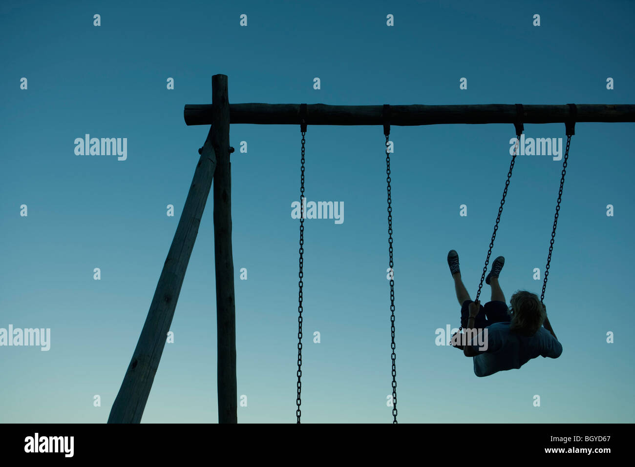 Young man swinging on swing set, backlit Stock Photo - Alamy