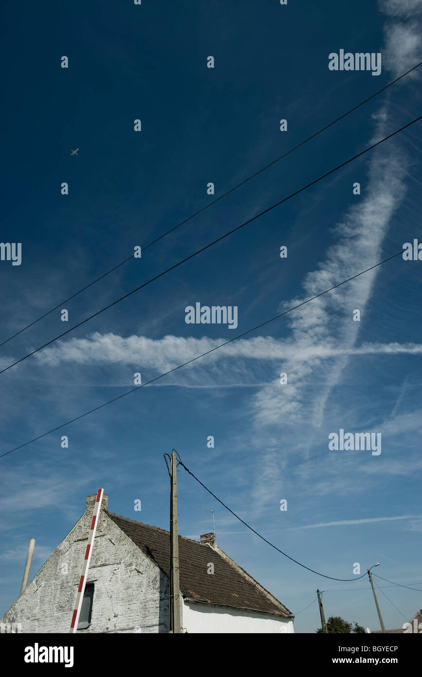 Vapor trails and airplane in blue sky above rustic house Stock Photo