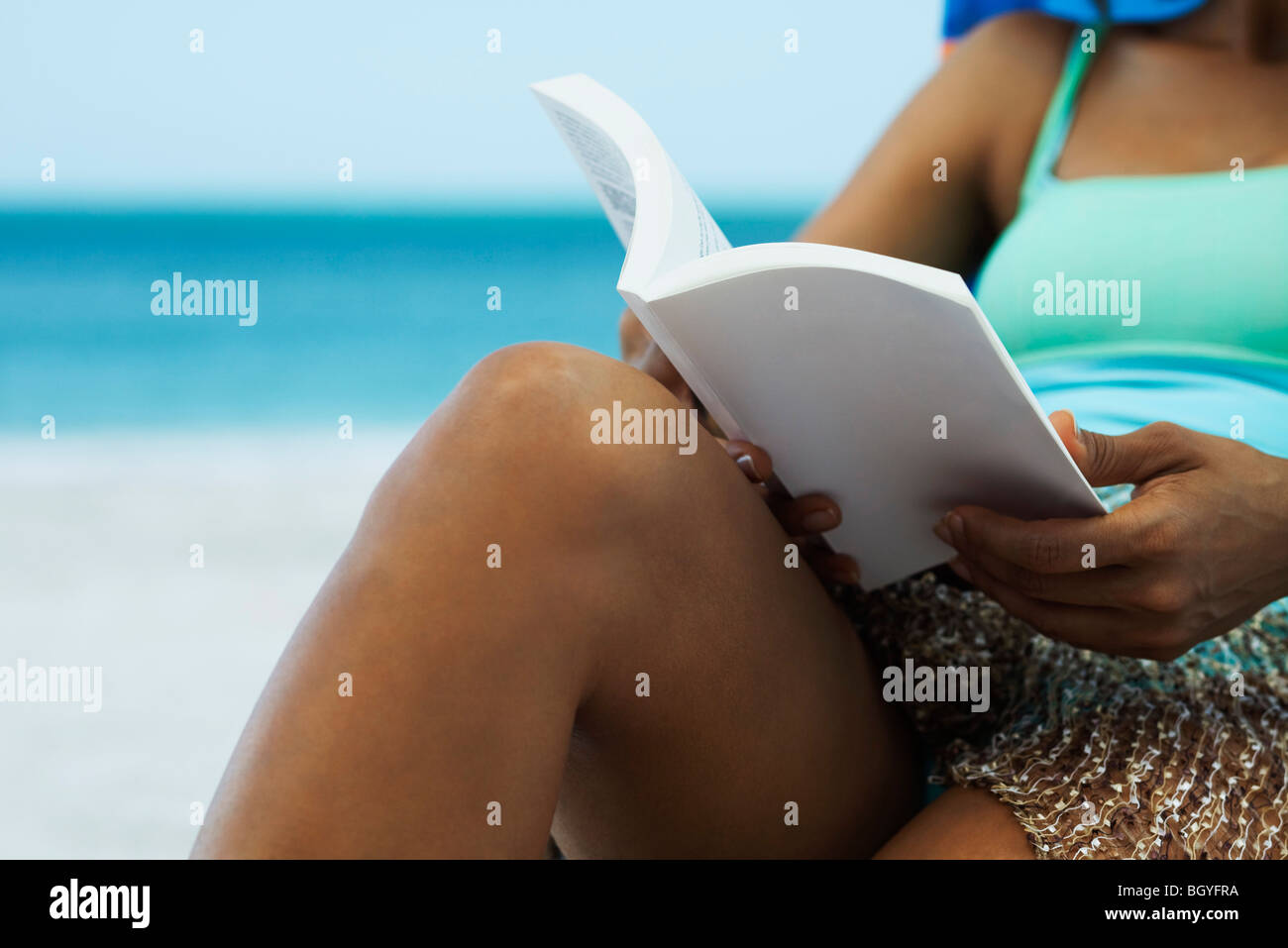 Woman reading book on beach, cropped Stock Photo
