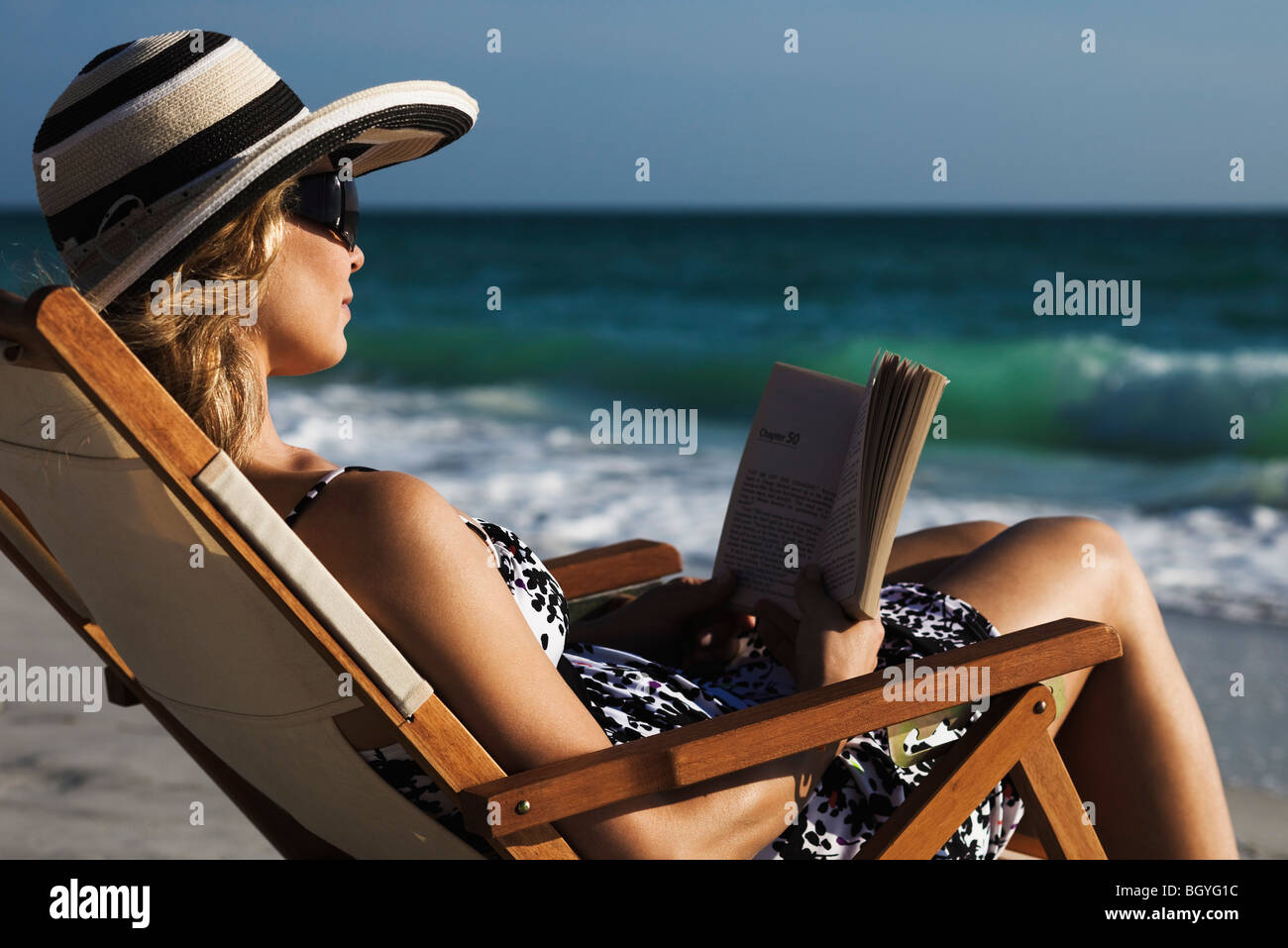Woman relaxing in deckchair at beach, reading book Stock Photo