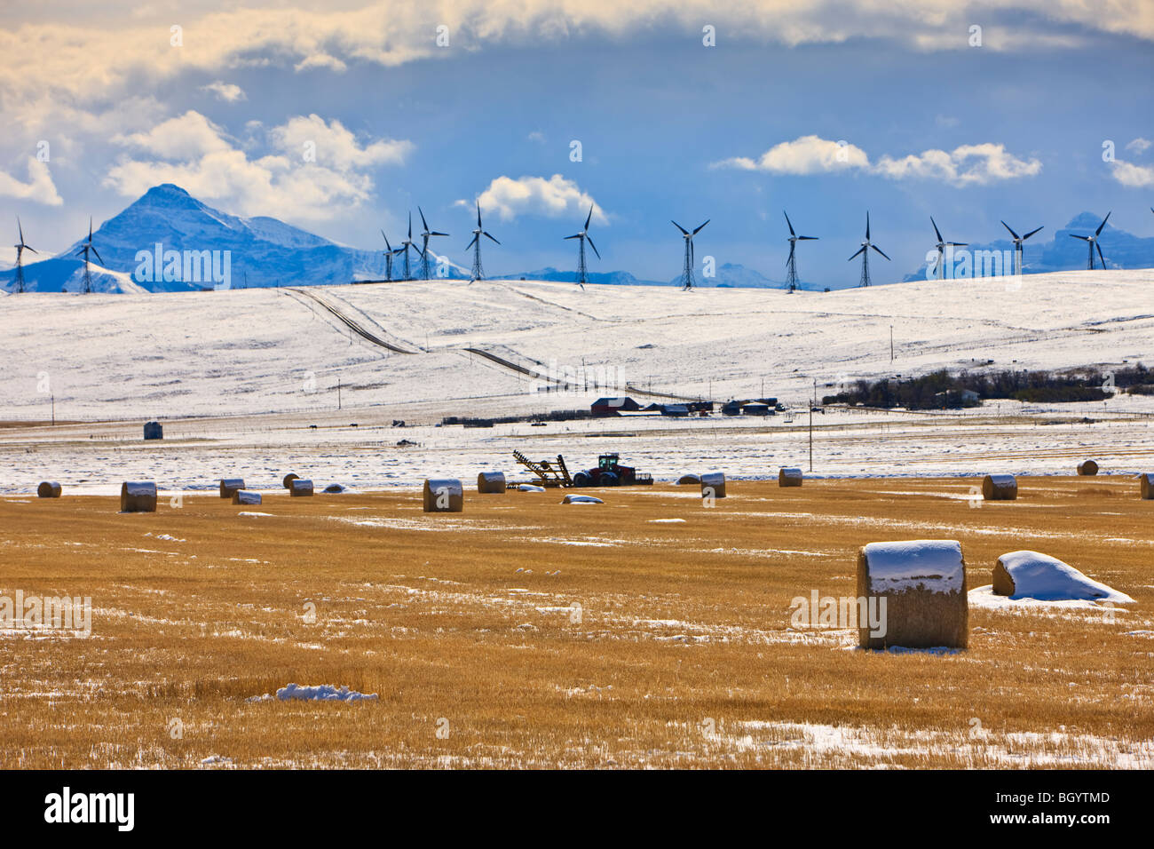 Hay bales covered in snow in Cowley backdropped by snowcovered mountains and windmills in Southern Alberta, Canada. Stock Photo