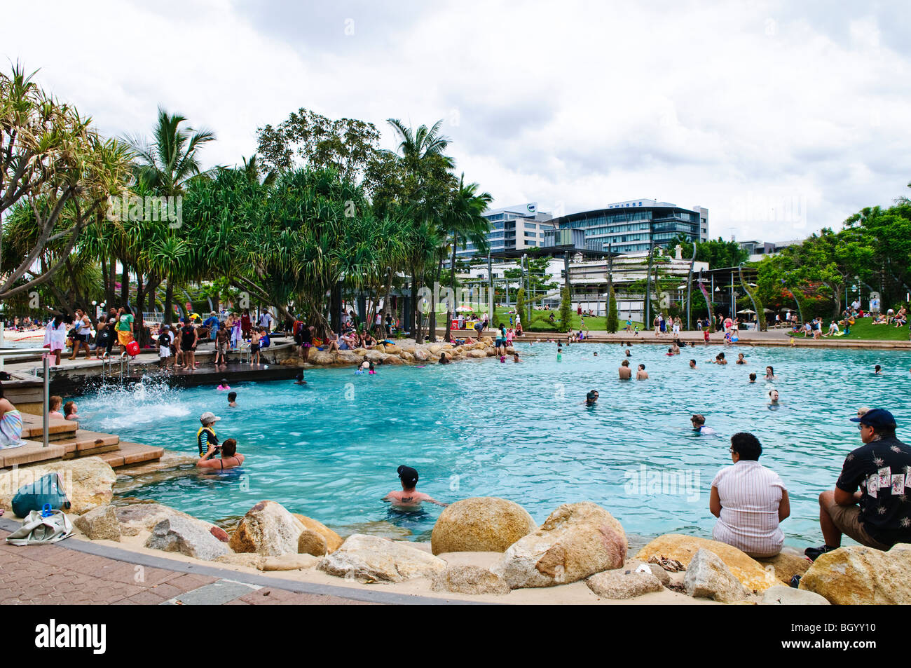 Southbank Parklands Beach And Lagoon Brisbane Australia // BRISBANE, Australia — Crowds enjoy the beach at Southbank, Brisbane's inner city beach, located along the Brisbane River. This popular urban oasis features a man-made lagoon, sandy beach, and lush parklands, offering locals and tourists a refreshing escape within the heart of the city. Southbank Parklands, developed on the site of World Expo '88, has become one of Brisbane's most visited leisure destinations since opening to the public in 1992. The area forms part of Brisbane's Cultural Precinct, situated near the Queensland Museum and Stock Photo