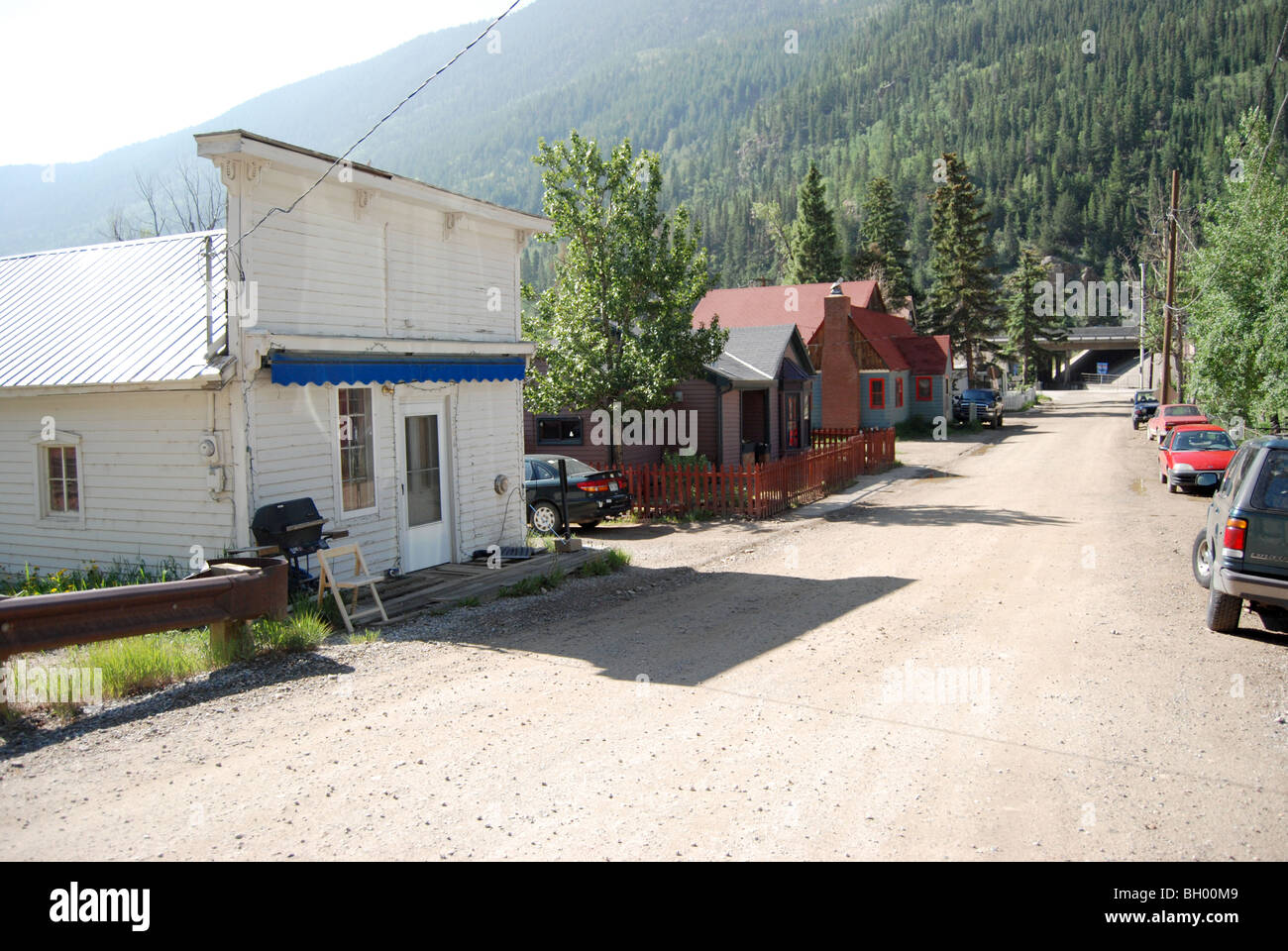 a view down dirt road street with houses and cars lining street in the