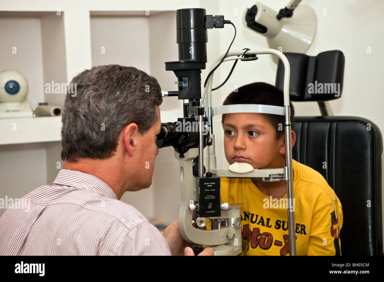 Optometrist using biomicroscope with a slit lamp to examine eye of 8 year old Hispanic boy. MR  © Myrleen Pearson Stock Photo