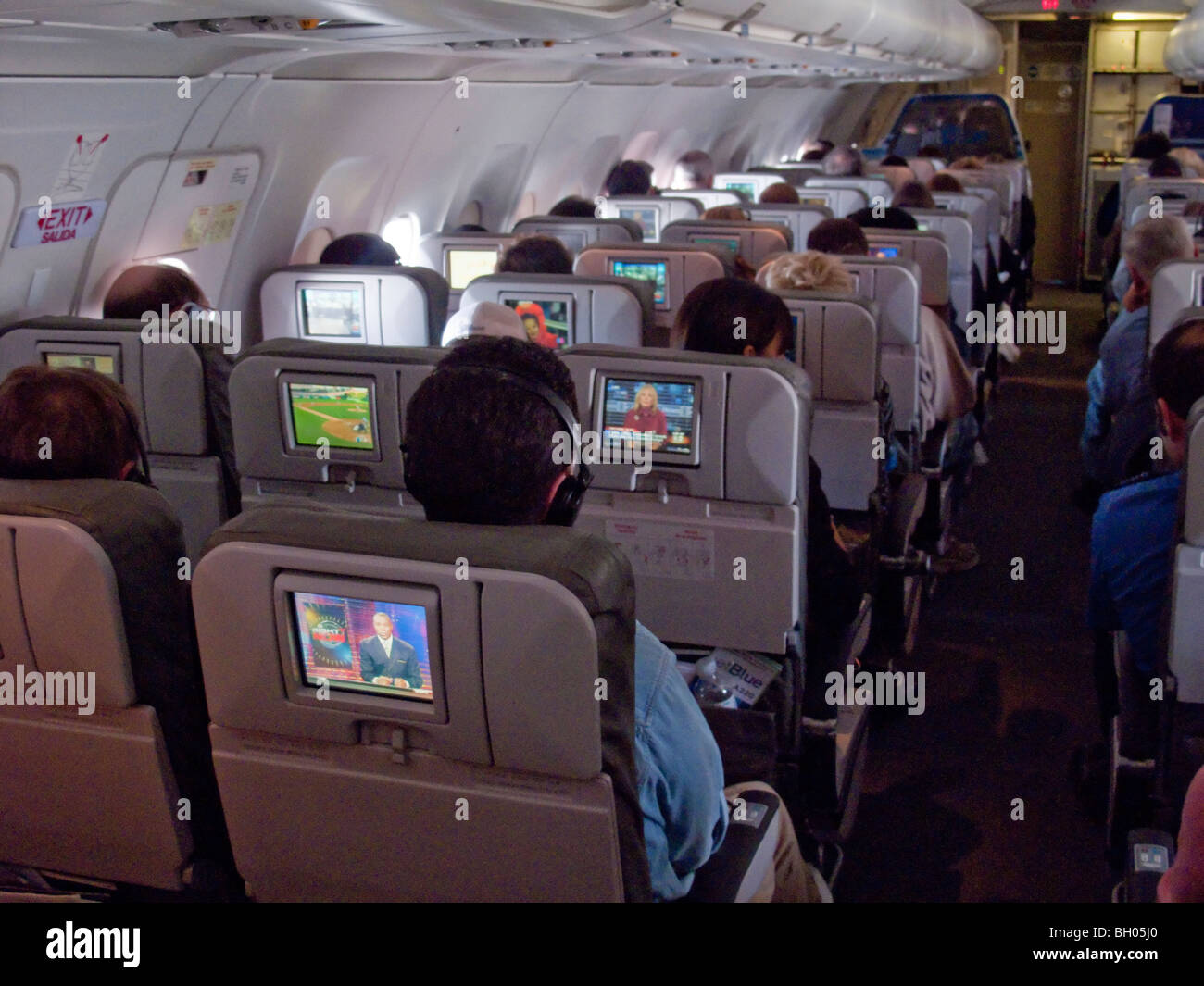 Airline cabin passengers enjoy in-flight television entertainment on individual screens at their seats. Stock Photo