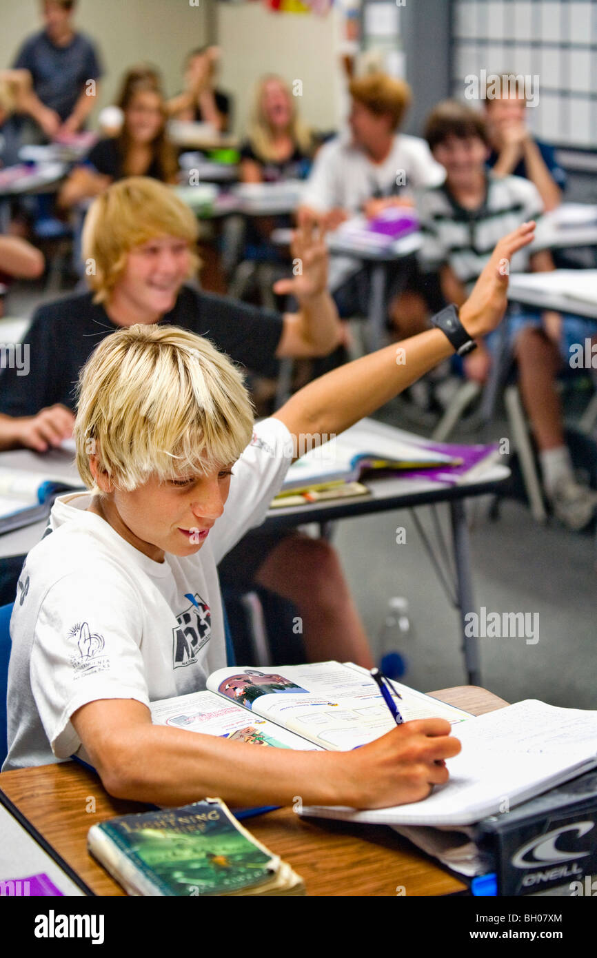A blonde, enthusiastic eight-grade boy holds up his hand to answer a question in class at a Southern California middle school. Stock Photo